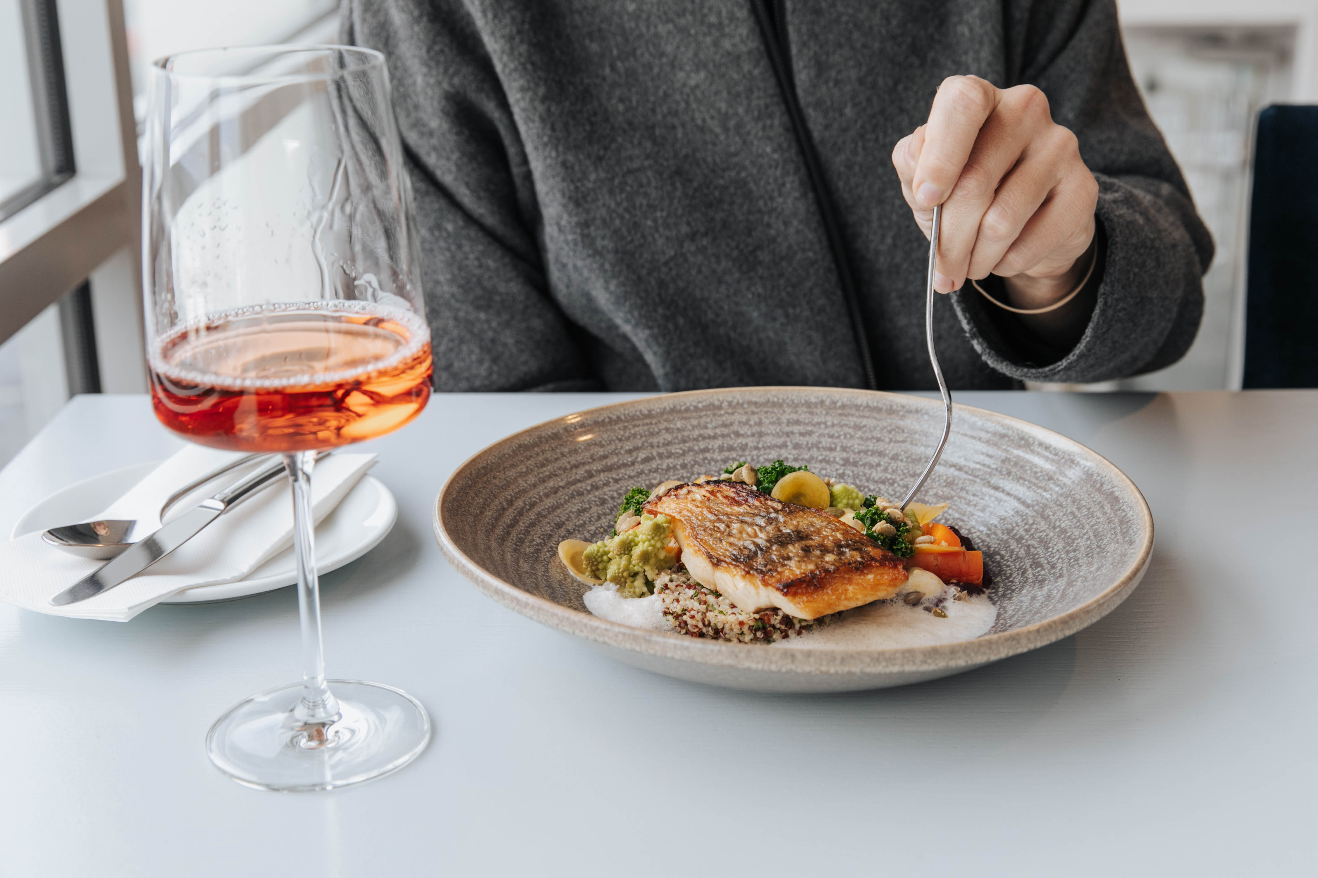 Woman sitting at the Tītī, St Clair. restaurant with a glass of wine and wild baked salmon